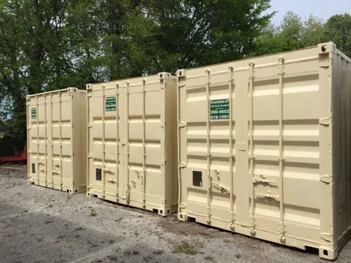 Three tan mobile storage containers lined up along a tree line